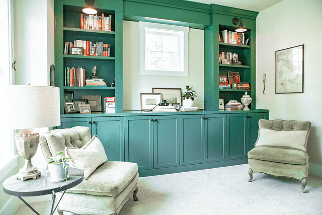 A home study with a green, built-in bookcase and two antique chairs.
